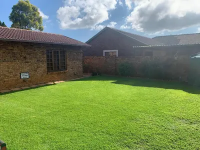 a yard with a brick wall and green grass at Dobbs Lodge in Centurion