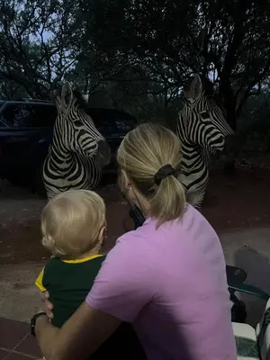 a woman holding a baby looking at two zebras at Tranquil Bush Cottage at Kruger in Marloth Park