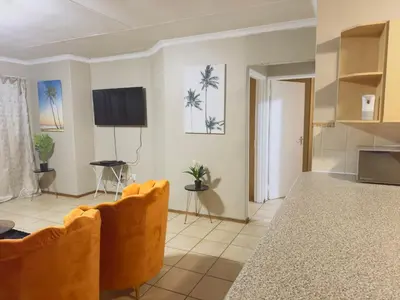 a living room with orange chairs and a flat screen tv at Luxury two bedrooms apartment in Witbank overnight accommodation in Witbank
