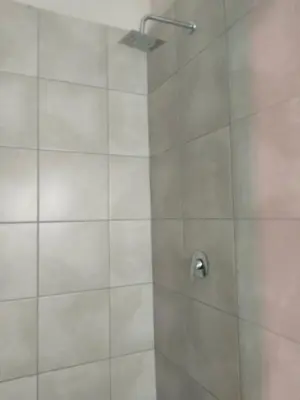 a shower with a glass door with a shower head at Rasesa Guesthouse Block V in Soshanguve