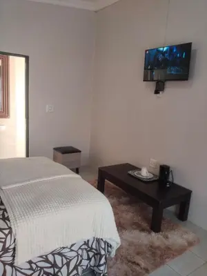 a bedroom with a bed and a table with a tv on the wall at Rasesa Guesthouse Block V in Soshanguve
