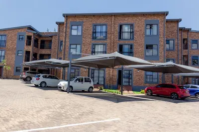 a parking lot with parked cars and umbrellas in front of a building at A spacious 1bedroom apartment in the heart of Kempton Park in Kempton Park