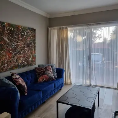 a living room with a blue couch and a large window at Kruin suite in Pretoria