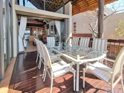 a glass table and white chairs on a balcony at Buffalo Game Lodge in Warmbaths
