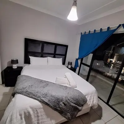 a bedroom with a large bed and a blue curtain at The Bylde Crystal Lagoon Apartment in Pretoria