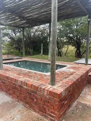 a brick retaining wall around a swimming pool with a roof at Dinokeng Bush Cabin in Hammanskraal