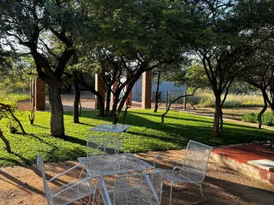 a table and chairs in a park with trees at Dinokeng Bush Cabin in Hammanskraal