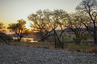 a sunset over a field with trees and a river at Luxury & Wildlife Mlambo Lodge Mjejane in Hectorspruit