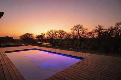 a swimming pool on a deck with a sunset in the background at Luxury & Wildlife Mlambo Lodge Mjejane in Hectorspruit