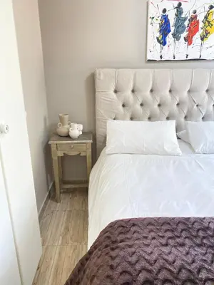 a bedroom with a white bed and a table with a picture at Cosy Room steps from the lake- short term stay in Benoni
