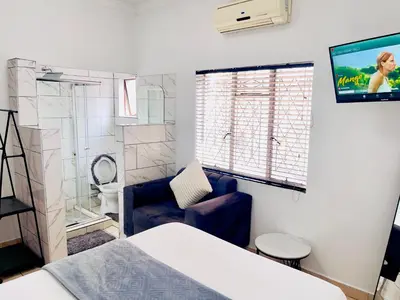 a room with a bed and a tv and a couch at Genza Guesthouse in Pretoria in Pretoria