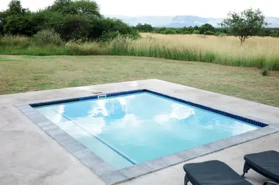 a swimming pool in a yard with two chairs at Amani Lodge - Villa 81 in Warmbaths