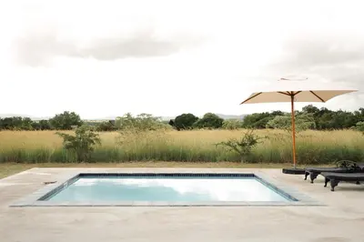 a swimming pool with an umbrella and two benches at Amani Lodge - Villa 81 in Warmbaths