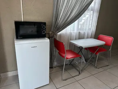 a tv on top of a refrigerator with a table and chairs at Nkandla Yethu Guest House in Nelspruit