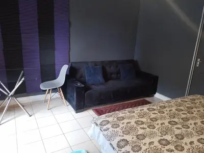 a black couch in a room with a bed and a chair at Aloha Menlyn Lodge in Pretoria