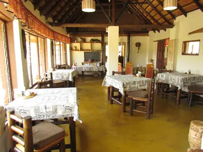 a dining room with tables and chairs and windows at Thokozani Lodge in White River