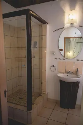 a bathroom with a shower and a sink and a mirror at Thokozani Lodge in White River