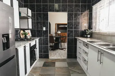 a kitchen with black tiled walls and white cabinets at Basambilu Guesthouse in Kempton Park