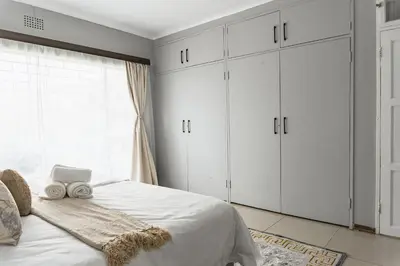 a bedroom with a bed with white cabinets and a window at Basambilu Guesthouse in Kempton Park