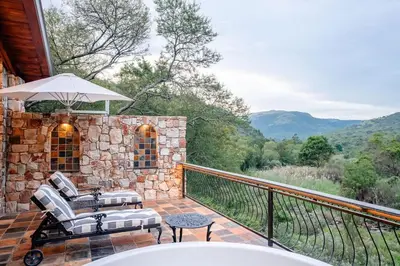 a patio with a chair and an umbrella on a balcony at Private luxurious suite on Heysbrook Estate halfway to Kruger National Park in Waterval-Onder