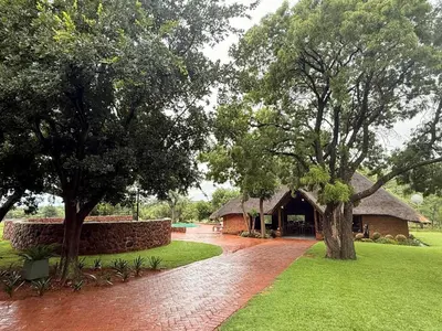 a building with a brick path and trees in front at Welgedacht Lodge in Cullinan