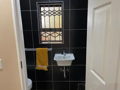 a black tiled bathroom with a sink and a window at Private Room with patio 2 in Mokopane