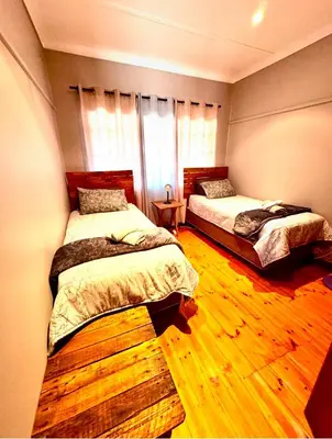 a bedroom with two beds and a wooden floor at Stone Cottage in Waterval Boven