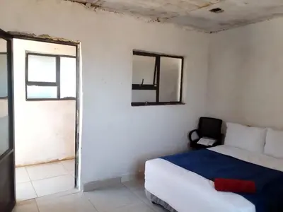 a white bedroom with a bed and a window at Mokoena Village guesthouse in Akasia