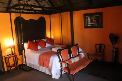 a bedroom with a bed with orange walls and two chairs at Makarios Lodge in Polokwane