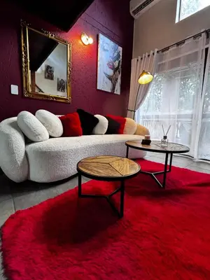 a living room with a couch and two tables on a red rug at The KinkyKabin in Sandton