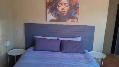 a bed with a blue headboard with a painting above it at Comfy at Sosha in Soshanguve