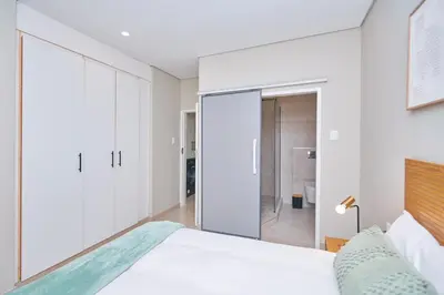 a bedroom with white walls and a bed with a glass door at La Genèse - S507 at Glen Park in Pretoria
