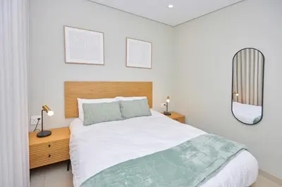 a white bedroom with a large bed and a mirror at La Genèse - S507 at Glen Park in Pretoria