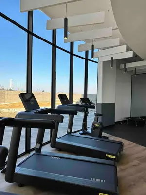 a row of treadmills in a gym with large windows at Explore Ellipse - Emerald Studio in Midrand