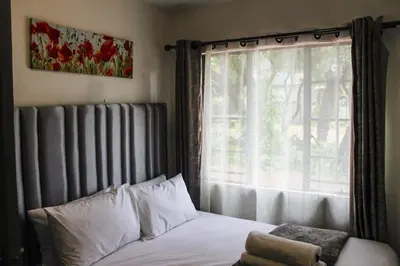 a bedroom with a bed and a window with white pillows at LOSKOP HOSPITALITY at TOLEDO APARTMENTS in Pretoria