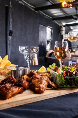 a cutting board with chicken and salad and glasses of wine at Empfunweni Guesthouse in Matsulu
