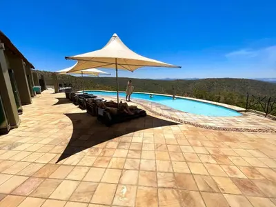 a man standing next to a swimming pool with an umbrella at RoiSan Private Game Lodge in Rooiberg