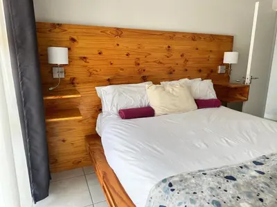 a bedroom with a white bed with a wooden headboard at regal retreat in the blyde in Pretoria