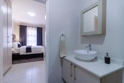 a white bathroom with a sink and a bed at First Floor 2 Beds Premium Suite in Midrand