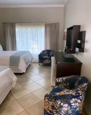 a hotel room with a bed and a tv and a chair at Destiny Lodge Cullinan in Cullinan