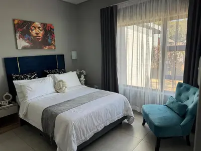 a bedroom with a bed and a chair and a window at Glowti Event & Guest House in Centurion