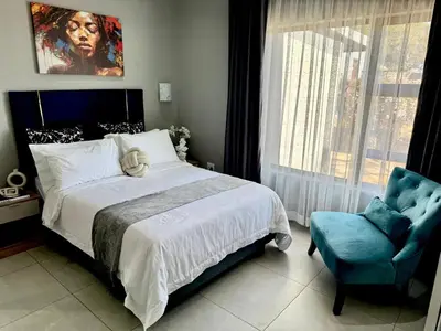 a bedroom with a large bed and a blue chair at Glowti Guest House in Centurion