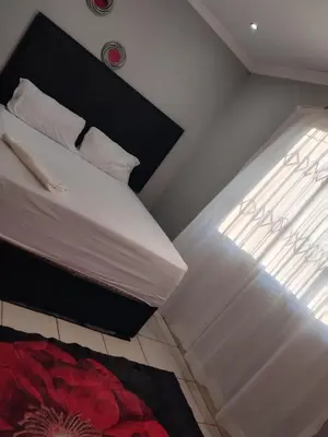 a bedroom with a bed with white sheets and a window at Queen Guest House in Pretoria