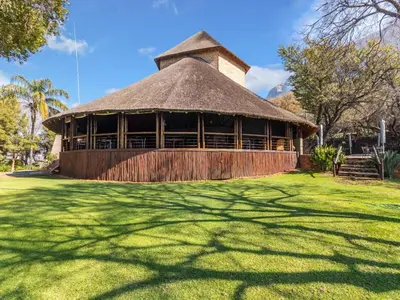 a large building with a straw roof on a grass field at Leopard Lodge in Hartbeespoort