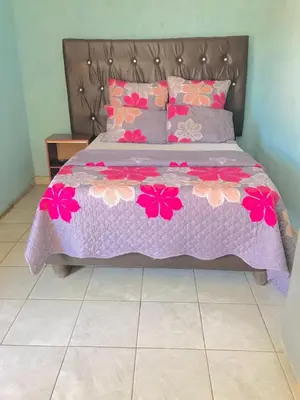 a bed with a purple comforter with pink flowers on it at Joyx BNB in Sibayeni