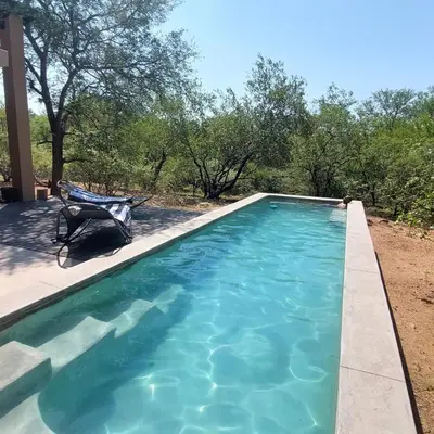 a swimming pool with a chair on a patio at Bush Serenity Studio in Marloth Park