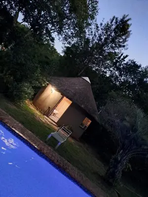 a small house with a thatch roof next to a pool at Afpak in Barberton