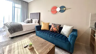 a living room with a blue couch and a bed at Menlyn Maine Residence - Studio Apartment in Pretoria