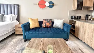 a living room with a blue couch and a kitchen at Menlyn Maine Residence - Studio Apartment in Pretoria