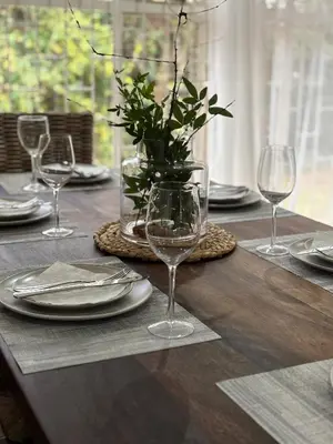 a wooden table with plates and glasses and a vase with flowers at DullVino Wellington House in Dullstroom